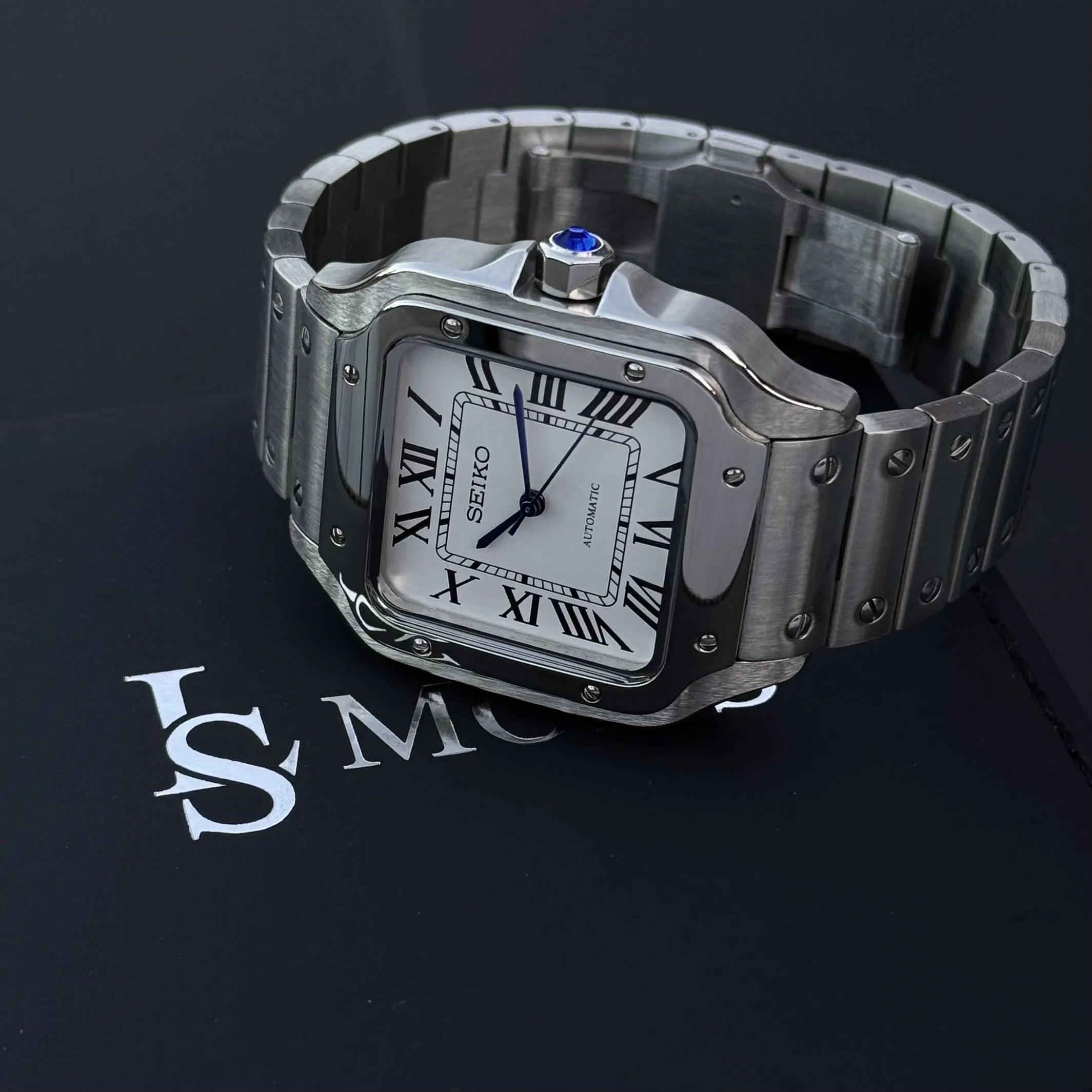 Montre Seiko Mod Santos cadran blanc à chiffres romains posée sur son écrin 